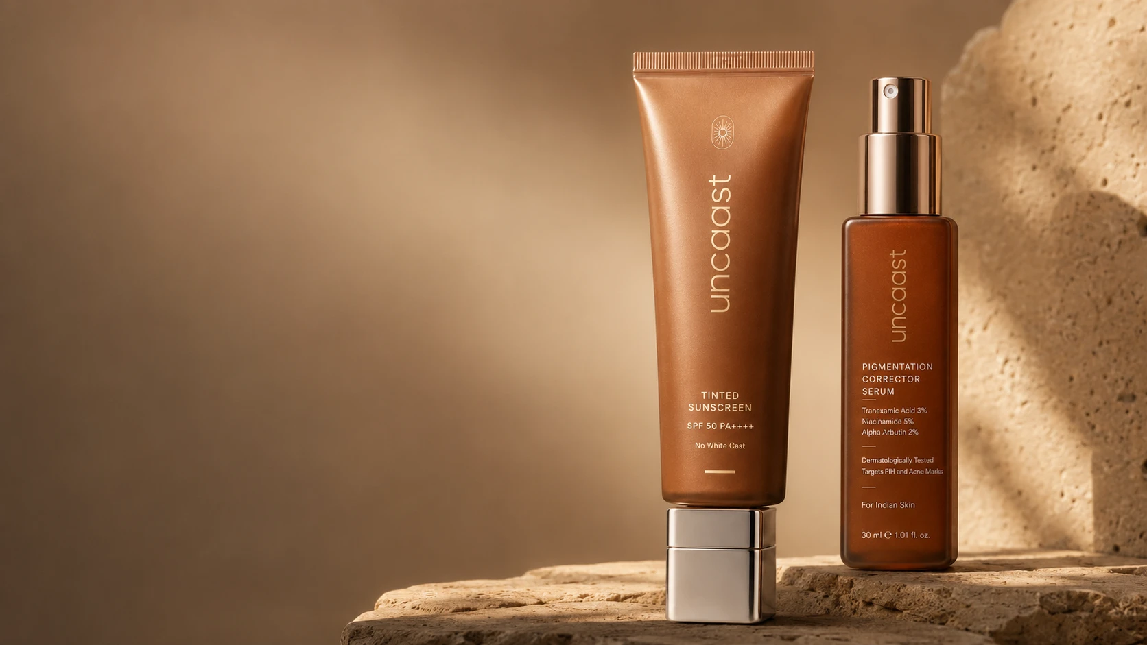 uncaast tinted sunscreen SPF 50 and pigmentation corrector serum for brown skin, standing together on warm stone in golden light