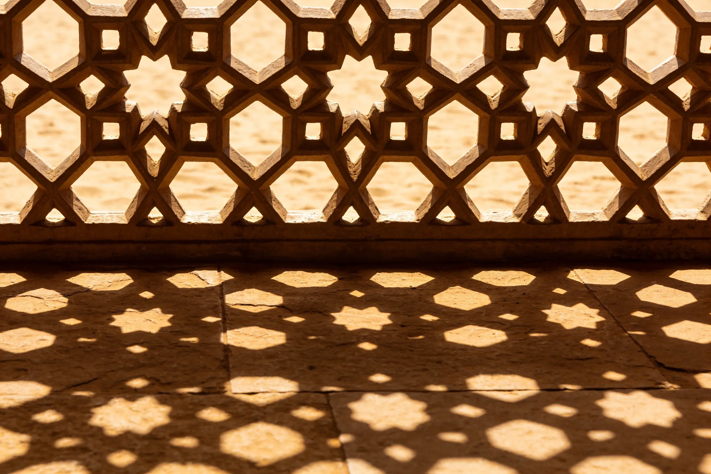 Sunlight passing through a carved Mughal jaali screen, casting a geometric lattice of shadow