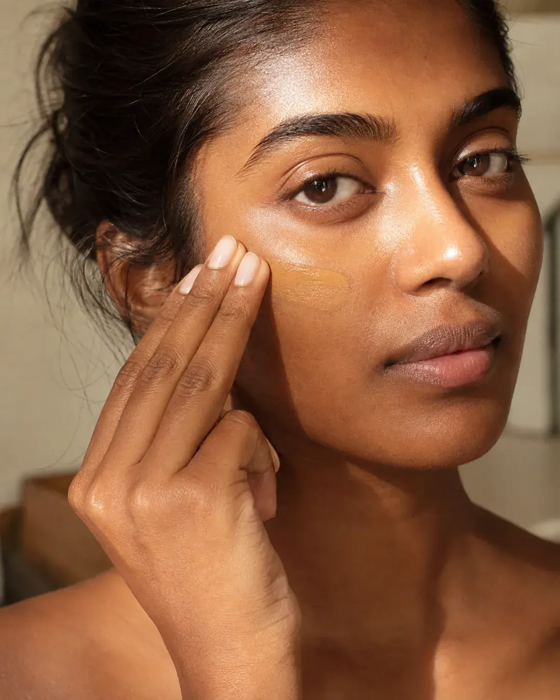 Woman with brown skin blending uncaast tinted sunscreen across her cheekbone
