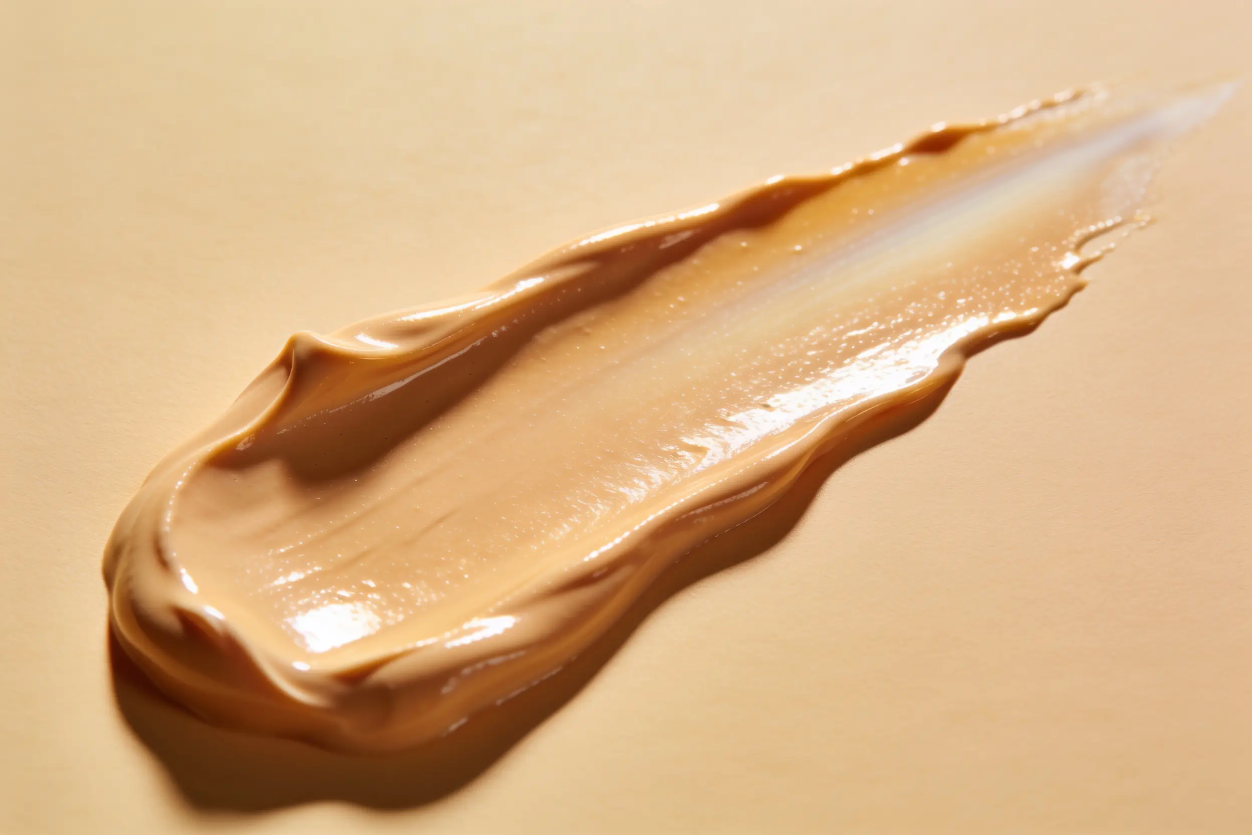 A swipe of golden tinted sunscreen cream showing its soft-satin finish and warm tone