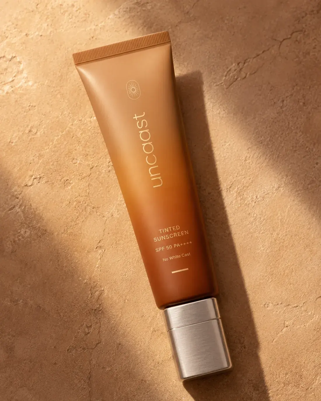 uncaast tinted sunscreen SPF 50 on warm travertine under palm shadows